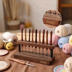 Könnte beinhalten: Ein Set aus Häkelnadeln mit Holzgriffen in einem dunklen Holzständer. Die Häkelnadeln haben unterschiedlich braune Griffe und silberne Metallspitzen. Der Ständer und eine einzelne Häkelnadel sind mit dem Namen "Emily" graviert.