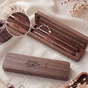 Könnte beinhalten: Eine dunkelbraune Holzaufbewahrungsbox mit Blumengravur und dem Namen Julia, die zwei Holzhäkelnadeln mit der Gravur Julia und den Größen 4.0mm und 5.0mm enthält. Die Häkelnadeln haben Metallspitzen und liegen in einem passenden Etui.