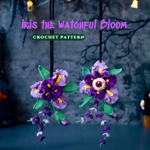 May include: Two crocheted iris flowers hanging from black cords, featuring purple and light purple petals, green leaves, and small dangling purple buds. One flower includes a realistic eyeball in the center. Text reads: IRIS THE WATCHFUL BLOOM CROCHET PATTERN.
