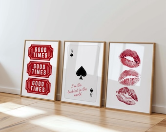 May include: Three framed art prints leaning against a wall. The prints feature a red "Good Times" ticket design, an Ace of Spades playing card with text, and three red lip prints. The frames are a light wood color.