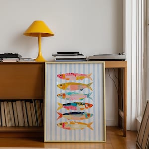 May include: A framed vertical art print featuring six stylized fish stacked in a column against a light blue and white vertical striped background. Each fish is rendered in a different color palette including pink, yellow, teal, and orange with patterns.