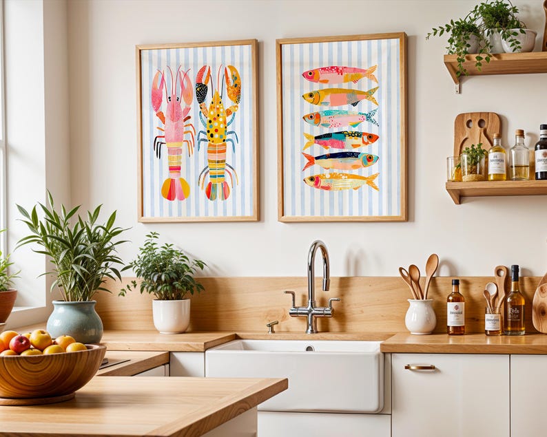 May include: Two framed wall art prints featuring colorful marine life illustrations. The left print displays two stylized lobsters, while the right print shows a vertical stack of six multi-colored fish, both set against a light blue striped background.