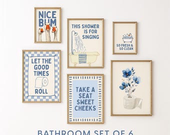 May include: A set of six framed bathroom art prints with gold frames. The prints feature whimsical illustrations and text, including phrases like "Nice Bum" and "Take a Seat Sweet Cheeks." The overall color scheme is blue and cream.