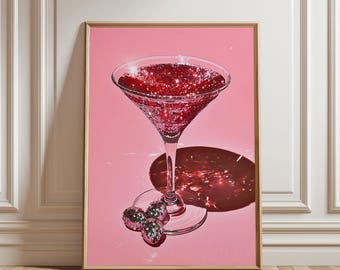 May include: A framed print featuring a martini glass filled with red glitter, casting a shadow on a pink background. Three small, glitter-covered spheres are at the base of the glass. The artwork is set against a white wall and wooden floor.