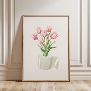Puede incluir: Impresión artística en acuarela que representa un ramo de tulipanes rosas en un rollo de papel higiénico. La obra de arte está enmarcada en un marco de madera marrón claro y sobre un fondo neutro. Los tulipanes tienen tallos y hojas verdes.
