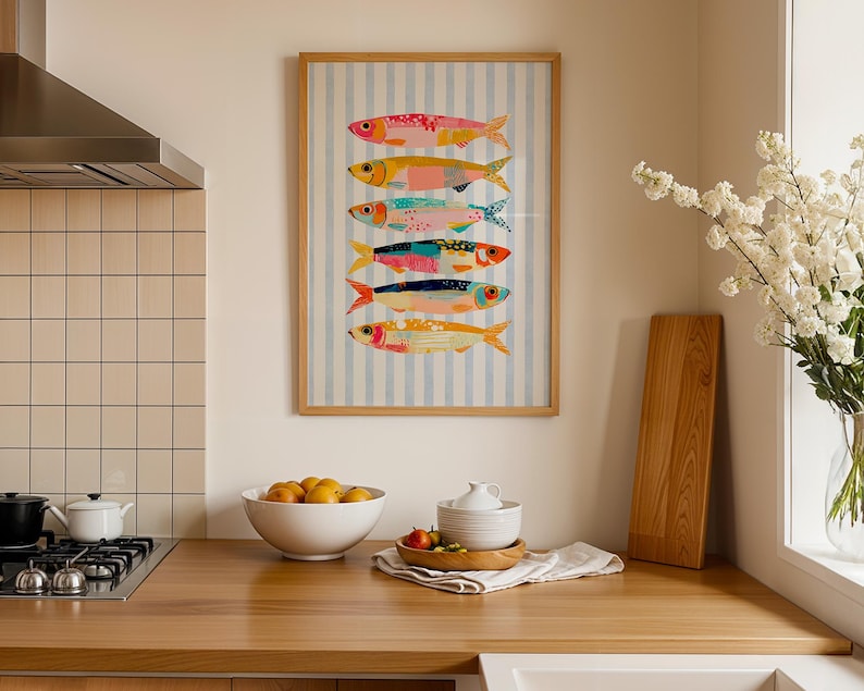 May include: A framed vertical wall art print featuring six stylized fish stacked in a column against a light blue and white vertical striped background. The fish are rendered in various bright colors including pink, yellow, teal, and orange.