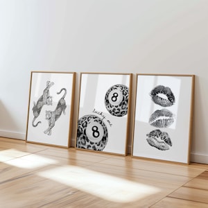 Op de afbeelding: Drie ingelijste kunstdrukken met een neutraal kleurenpalet. De prints tonen een luipaardontwerp, een poolbal met het nummer 8 en lipafdrukken. De poolbalprint bevat de tekst "lucky me". De frames hebben een natuurlijke houten afwerking.