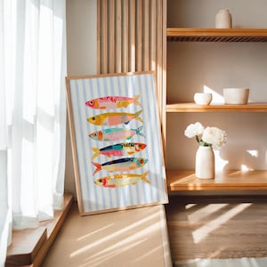 May include: A framed art print featuring six stylized fish stacked vertically, each with unique colorful patterns and textures, set against a light blue and white vertical striped background. The fish are rendered in shades of pink, yellow, teal, and orange.