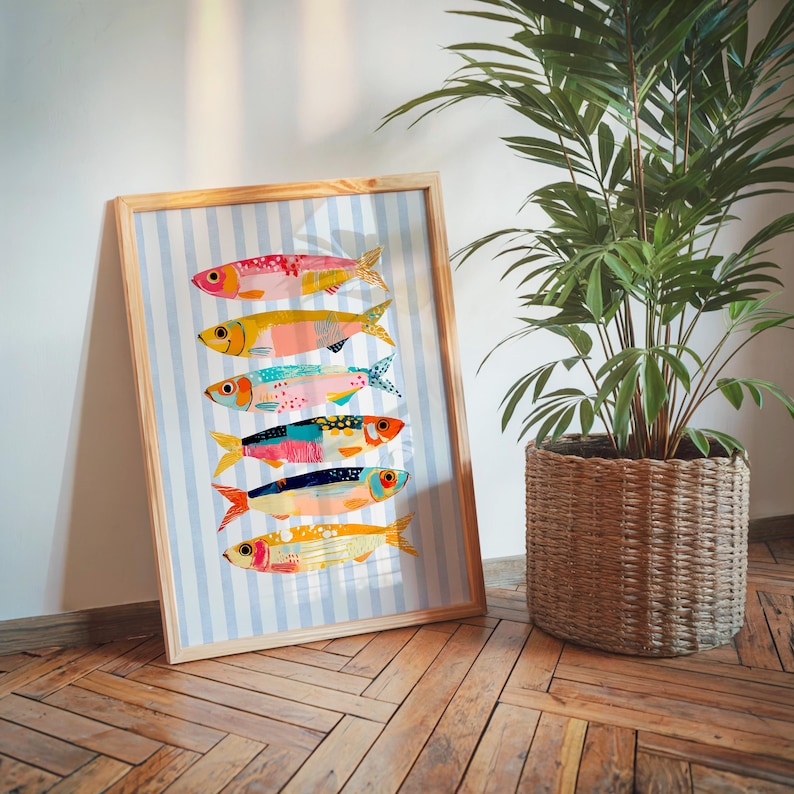 May include: A framed art print featuring six stylized fish stacked vertically against a light blue and white vertical striped background. Each fish displays a unique combination of vibrant colors, including pink, yellow, teal, orange, and blue patterns.