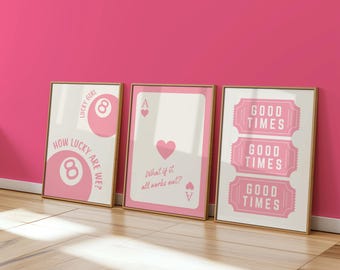 May include: Three framed art prints with gold frames. The prints feature pink and white designs with text. One print has an 8-ball and the words "How lucky are we?" Another shows a playing card with a heart and the text "What if it all works out?" The third print says "Good Times".