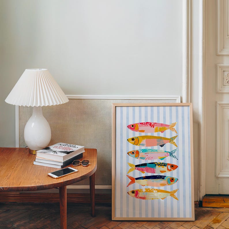 May include: A framed vertical print featuring six stylized fish stacked horizontally, each with unique colorful patterns, set against a light blue and white vertical striped background. The artwork is displayed in a light wood frame.