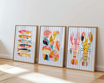 May include: Three framed vertical art prints featuring marine life illustrations on a light blue and white striped background. The first print shows six colorful fish, the second displays various seashells, and the third depicts two lobsters.
