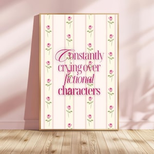 Puede incluir: Un cartel enmarcado con el texto "Constantly crying over fictional characters". El fondo es crema con rayas rosas e ilustraciones de rosas. El marco es dorado. El cartel está sobre un suelo de madera.