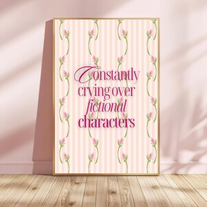 Puede incluir: Impresión enmarcada con un fondo a rayas rosas y blancas, con el texto "Constantly crying over fictional characters" en cursiva. Decorada con detalles florales rosas y un marco dorado.