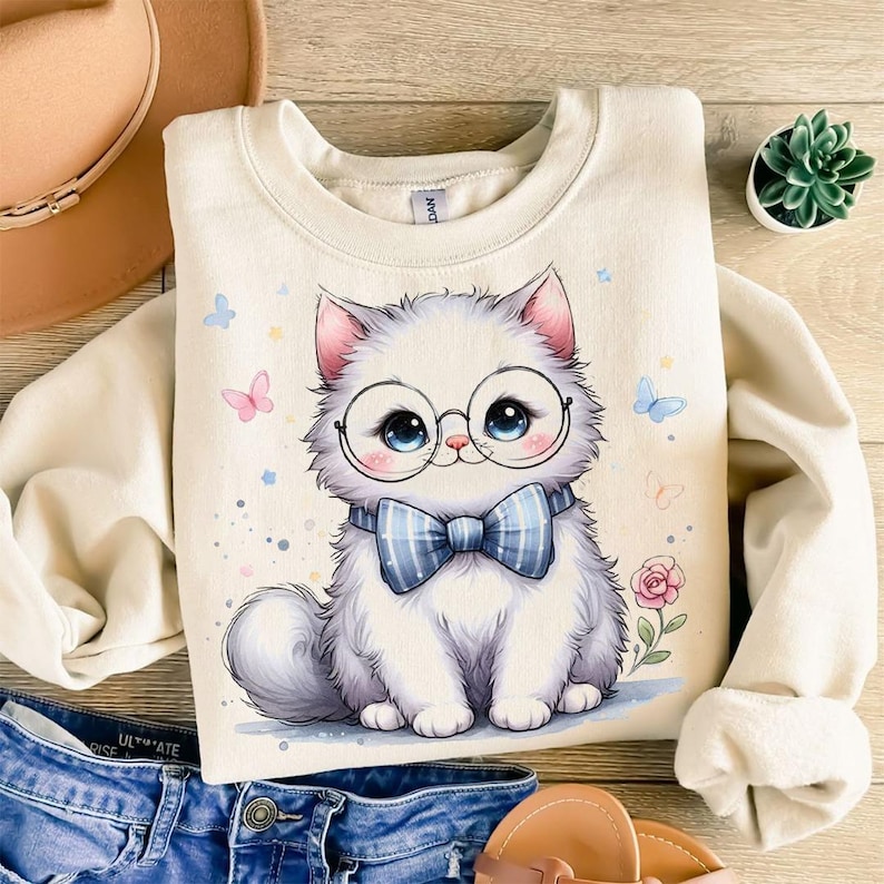 May include: Cream-colored sweatshirt featuring a cartoon cat wearing glasses and a blue bow tie. The cat has large blue eyes and is surrounded by butterflies and flowers. A cute and whimsical design.