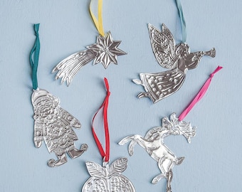 May include: A collection of silver-colored Christmas ornaments with colorful ribbons. The ornaments include a star with a comet tail, an angel playing a trumpet, a Santa Claus figure, a pomegranate, and a reindeer. The ornaments are on a light blue background.