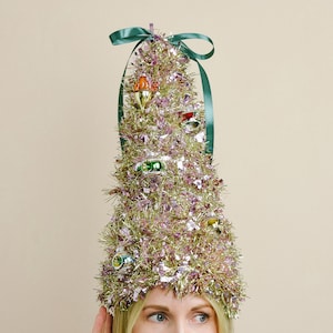 Puede incluir: Un sombrero de árbol de Navidad caprichoso hecho de oropel dorado y rosa, adornado con coloridos adornos en miniatura y una cinta verde. El tocado festivo está diseñado para ser usado en la cabeza, perfecto para celebraciones navideñas.
