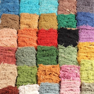May include: A selection of colourful, textured ribbon spools in shades of blue, green, orange, and pink. The ribbon has a frayed, woven appearance, suitable for crafts and embellishments.