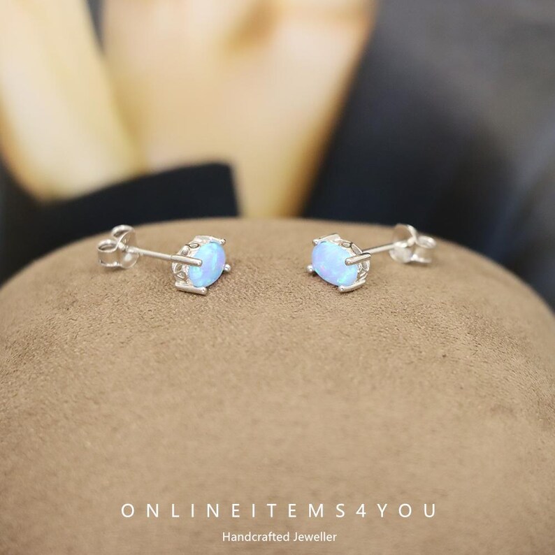 May include: A pair of silver stud earrings with oval, light blue opal stones. The earrings are set in a four-prong setting. The text "ONLINEITEMS4YOU Handcrafted Jeweller" is at the bottom of the image.
