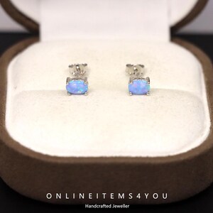 May include: A pair of oval-shaped opal stud earrings set in silver. The earrings are displayed inside a brown jewelry box with a white interior. The text "ONLINEITEMS4YOU Handcrafted Jeweller" is at the bottom.