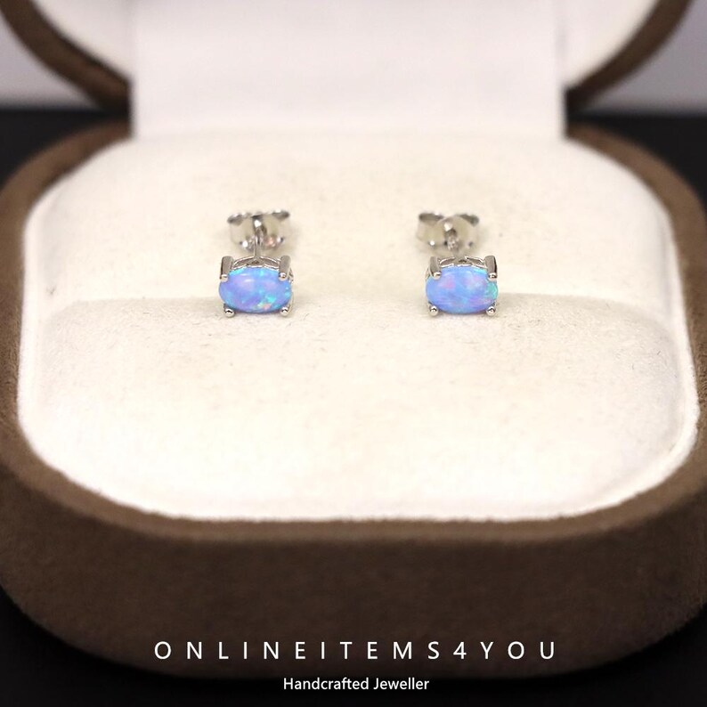 May include: A pair of oval-shaped opal stud earrings set in silver. The earrings are displayed inside a brown jewelry box with a white interior. The text "ONLINEITEMS4YOU Handcrafted Jeweller" is at the bottom.