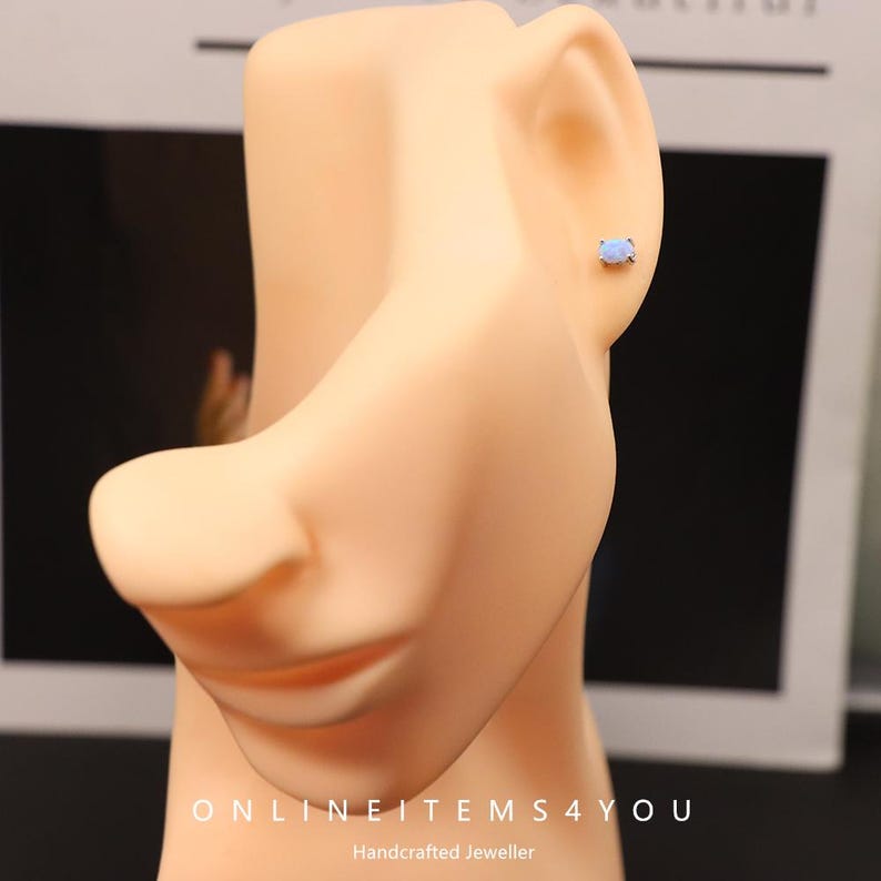 May include: A light blue oval gemstone stud earring on a mannequin. The earring is set in a silver metal. The mannequin has a light skin tone. The text "ONLINEITEMS4YOU" and "Handcrafted Jeweller" are visible.