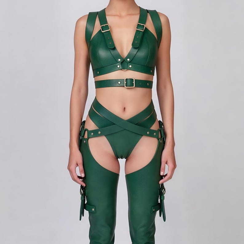 May include: A green leather harness set featuring a bra top, waist belt, and high-waisted bottoms with attached chaps. The set includes adjustable straps and metal buckle closures. The outfit is designed with a form-fitting silhouette.