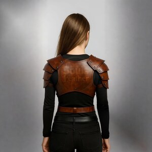 May include: Brown leather shoulder armor with the text "Soul Leather" embossed on the back. The armor has a series of rivets and is worn over a black long-sleeved shirt. A brown belt is also visible.