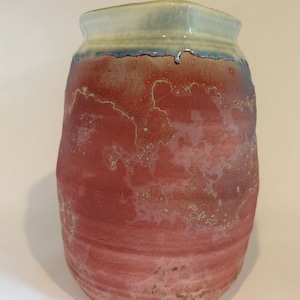 May include: A red ceramic vase with a white rim and a mottled glaze. The vase has a rounded shape and a textured surface.