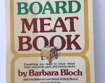 May include: A vintage cookbook titled "The Meat Board Meat Book" by Barbara Bloch with an introduction by Julia Child. The cover features a yellow background with a brown wooden cutting board and knives.