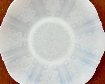 May include: A white, ornate glass plate with a ruffled edge. The plate features a detailed, embossed floral pattern across its surface. The design is centered and radiates outwards, creating a delicate and elegant aesthetic.