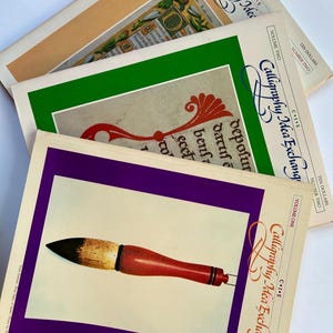 May include: A stack of vintage "Calligraphy Idea Exchange" magazines. The covers feature calligraphy tools and examples, with a red and brown brush on a purple background. Other covers have green and tan borders.