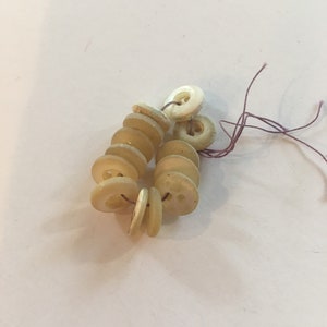 May include: A group of off-white plastic buttons with two holes each, strung together with a purple thread.