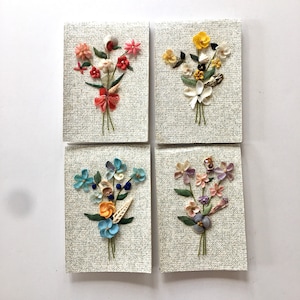 May include: Four framed wall art pieces featuring bouquets of flowers made from seashells. Each piece has a different color scheme: pink, white, blue, and purple.