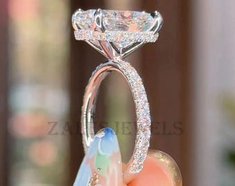 May include: A diamond ring featuring a large, rectangular-cut central stone, surrounded by a halo of smaller diamonds. The band is also encrusted with diamonds. The ring is held up by a person. The text "Zales Jewels" is visible.