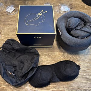 May include: A travel set including a navy blue box with a gold design, a gray neck pillow, a black eye mask, and a black drawstring bag. The box has the text "ALVOC TRAVEL PILLOW". The eye mask is black and contoured.