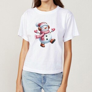 Pu&ograve; includere: T-shirt bianca con una grafica di pupazzo di neve allegro. Il pupazzo di neve indossa una sciarpa, un cappello e guanti a righe rosa e bianche, e stivali marroni. Il pupazzo di neve sorride e balla. Design festivo.