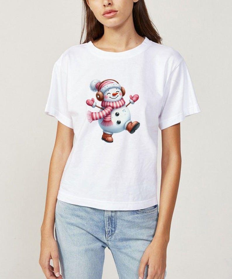 Pu&ograve; includere: T-shirt bianca con una grafica di pupazzo di neve allegro. Il pupazzo di neve indossa una sciarpa, un cappello e guanti a righe rosa e bianche, e stivali marroni. Il pupazzo di neve sorride e balla. Design festivo.