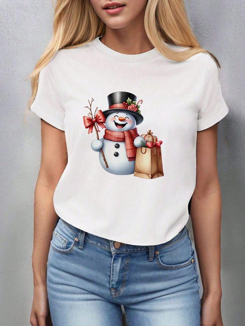 Pu&ograve; includere: T-shirt bianco con un allegro design a pupazzo di neve. Il pupazzo di neve indossa un cappello a cilindro nero, una sciarpa rossa e tiene in mano un rametto con un fiocco rosso. Un sacchetto di carta marrone con regali completa il look festivo.