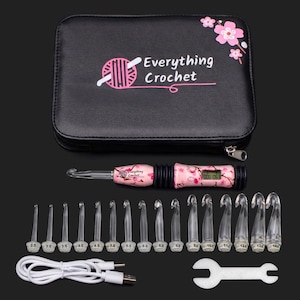 May include: A black zippered case with the text "Everything Crochet" and a pink floral design. The set includes a lighted crochet hook, multiple crochet hooks of varying sizes, a USB charging cable, and a small wrench.