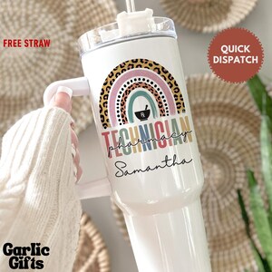May include: White tumbler with a handle and a clear lid, featuring a colorful rainbow design with a leopard print arch. The text "TECHNICIAN PHARMACY Samantha" is printed below the rainbow. A straw is included.