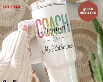 May include: White tumbler with a handle, featuring the words "COACH Volleyball" in colorful letters, a volleyball graphic, and the name "Ms. Katherine" in script. Includes a straw and lid.