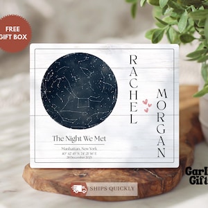 May include: A personalized wooden sign featuring a dark blue star map within a circle, with the names "Rachel" and "Morgan" vertically on either side. The text "The Night We Met" and location details are below the star map. The sign is on a wooden base.