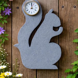 May include: A gray squirrel-shaped outdoor clock mounted on a wooden fence. The clock face is round with a gold-colored bezel and black numerals. The background includes flowers and greenery.