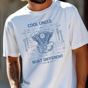 May include: White t-shirt featuring a blue blueprint design of a motorcycle engine, spanners, and the text "COOL UNCLE BUILT DIFFERENT". The shirt is made of a soft, comfortable material.