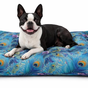 May include: A Boston Terrier dog rests on a rectangular pet bed. The bed features a vibrant peacock feather design in shades of blue, teal, and purple. The dog is black and white with a happy expression.