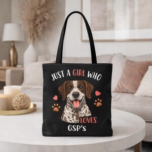 May include: Black tote bag featuring a German Shorthaired Pointer illustration with the text "JUST A GIRL WHO LOVES GSP'S". The design includes paw prints and hearts. The bag has black handles.