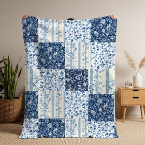 May include: A rectangular throw blanket featuring a patchwork design of alternating squares. The pattern consists of deep blue and white floral motifs, intricate botanical vines, and vertical striped sections on a cream-colored background.