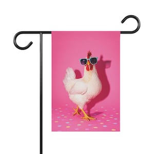 Puede incluir: Una bandera de jardín rectangular que muestra un pollo blanco con gafas de sol azul claro. El pollo está sobre una superficie rosa decorada con pequeños puntos multicolores sobre un fondo rosa vibrante y sólido, colgado de un soporte de metal negro.