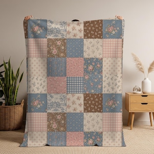 May include: A patchwork quilt with a variety of floral, gingham, and patterned squares in shades of blue, pink, brown, and cream. The quilt is held up by unseen hands, showcasing its design and colors.